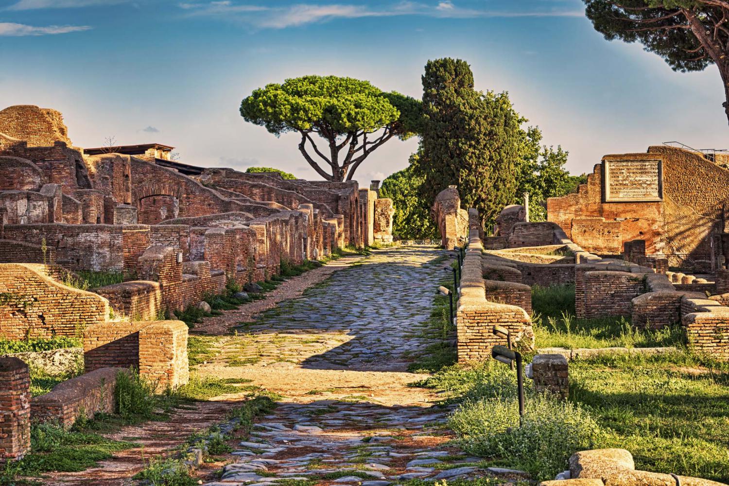  An ancient Roman street with a stone path and the ruins of buildings on either side, including a wooden funnel-shaped object.